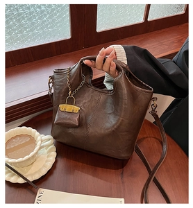 Detail of dark brown leather bucket bag with elegant gold chain charm and soft texture