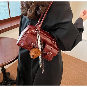 Detail of burgundy glossy leather bag with multiple buckled pockets and teddy charm