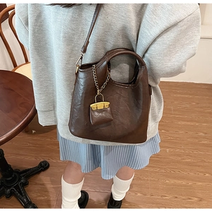 Detail of dark brown bucket bag with leather texture and mini purse pendant accessory
