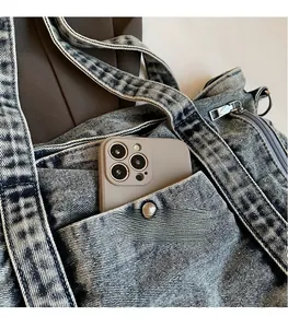 Detail of washed denim tote bag featuring external pocket with metal button and zip closure