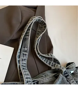 Detail of blue washed denim tote showing adjustable long strap and smooth metal zipper