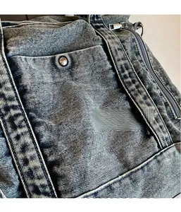 Detail of washed denim fabric with metallic rivets and zippers on a casual tote bag