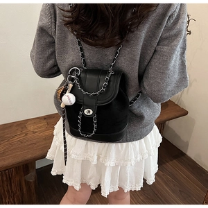 Detail of black quilted mini backpack featuring chain straps and a baseball pendant charm