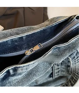 Detail of silver smooth metal zipper pull and washed denim fabric on the tote bag