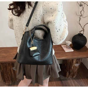 Minimalist black leather tote bag with gold chain micro pouch accessory shown on shoulder