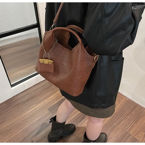 Brown leather tote bag featuring a miniature charm and gold chain detail on model