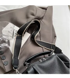 Detail of black lychee grain leather pillow bag with stylish black and white wide strap