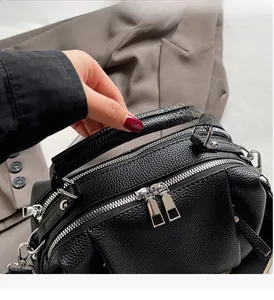 Detail of black pebbled leather handbag featuring dual silver zippers and sturdy top handle