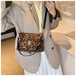 Detail of leopard print crossbody bag with metallic clasp worn with beige suit