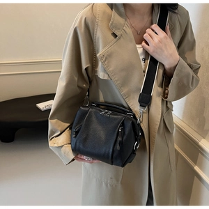 Detailed view of black pebbled leather crossbody bag with wide shoulder strap worn by model