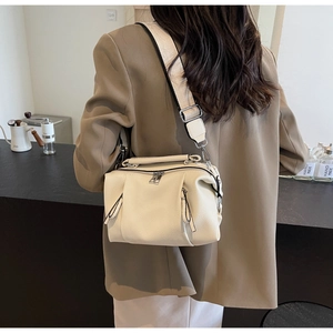 Detail of off-white lychee grain leather bag with wide strap worn by a model