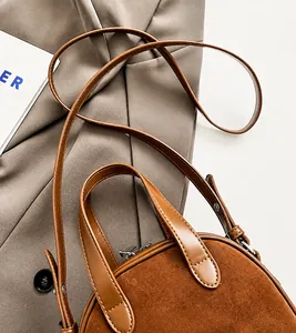 Detail van donkerbruine suède crossbodytas met lederen handvatten en zilveren hardware