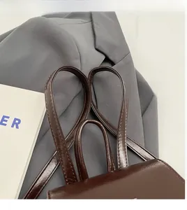 Détail du sac en similicuir marron montrant les bretelles et la poignée supérieure robuste