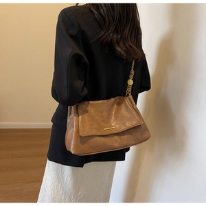 Detail of a brown leather shoulder bag with a gold metal bar closure and chain strap