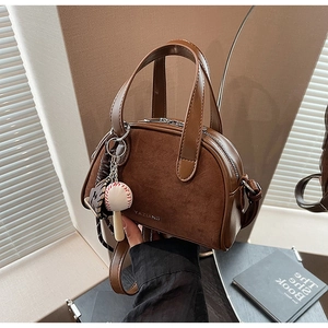 Detail van donkerbruine suède crossbodytas met baseballhangers en zilveren ritssluiting