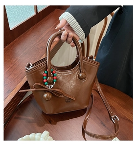 Détail d'un sac seau en cuir ciré marron avec un nœud décoratif et un accessoire en perles