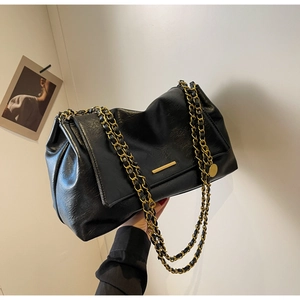Close-up of black leather handbag featuring gold metal chain strap and sleek metal accent