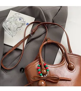 Détail d'un sac seau en cuir marron avec nœud posé sur une veste de blazer grise
