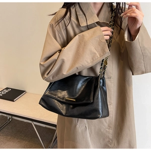 Detail of glossy black leather tote with gold buckle and metal chain strap on trench coat