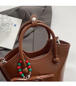Détail d'un sac à main en cuir marron brillant avec anses rondes et breloque en perles