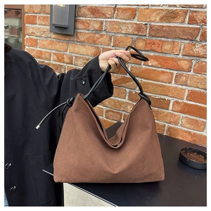 Gros plan sur un sac cabas en daim marron mat avec des poignées en corde noire et des nœuds