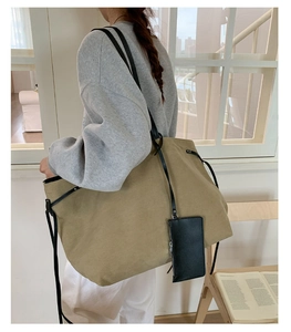 Dettaglio di una borsa tote grande in tela kaki con manici in pelle nera indossata