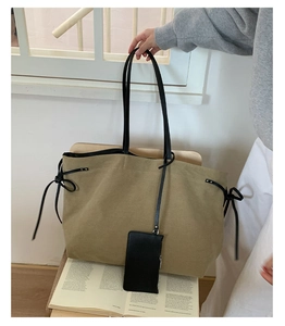 Dettaglio della borsa tote in tela kaki con manici in pelle nera e fiocchi laterali