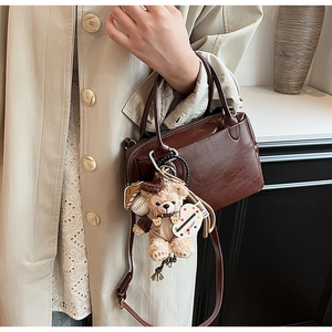 Détail du sac carré en cuir marron foncé avec texture litchi et breloque en peluche