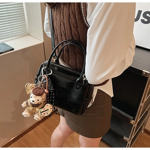 Détail du sac à main en cuir verni noir avec charm ours et finition élégante