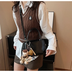 Détail d'un sac Boston noir brillant avec charms décoratifs et bandoulière réglable