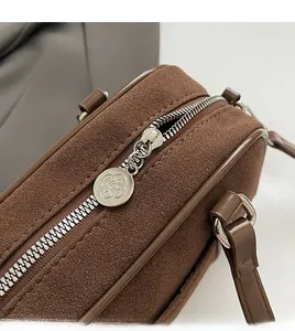 Detail of silver metal zipper and brand logo on brown matte bowling bag with suede texture