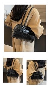 Detail view of glossy black faux leather shoulder bag with sleek metallic zipper and double straps