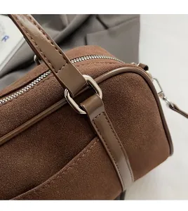 Detail of a dark brown suede barrel bag showing fine stitching and silver hardware