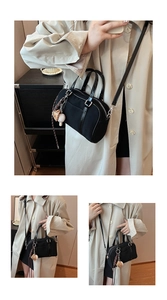 Détail du sac Boston noir avec garniture en cuir et pendentif baseball sur manteau beige