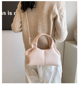 Detail view of beige ruched cloud bag with thin strap worn by model in soft light
