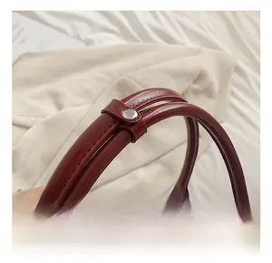 Detail of burgundy PU leather handbag with silver zipper and secure dual handle strap