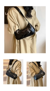 Detail of black half-moon underarm bag with glossy finish and punk metal buckles