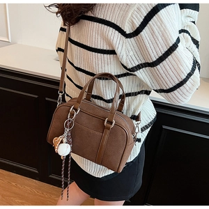 Brown matte Boston bag detail featuring a baseball pendant and adjustable shoulder strap