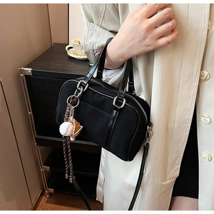 Close-up of black Boston bag with baseball glove charm and patent leather handles