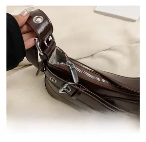 Détail d'un sac porté épaule en cuir marron brillant avec des œillets argentés