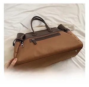 Detail of two-tone brown leather tote bag showing zippers and protective base rivets