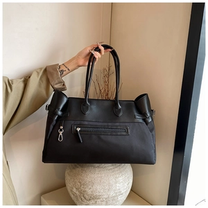 Detail of black nylon tote bag with leather straps and front zip pocket held by hand