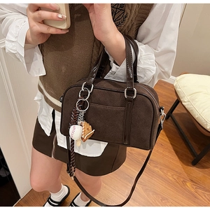Close-up of brown suede Boston bag with patent leather handles and baseball charm