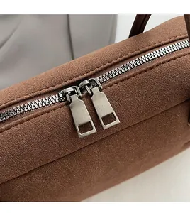 Details von zwei glatten Reißverschlüssen an einer braunen Zylinder-Wildledertasche