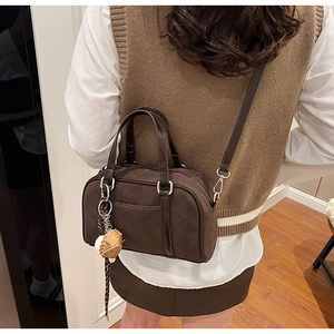 Detail of dark brown Boston bag in suede finish with baseball charm shown on model