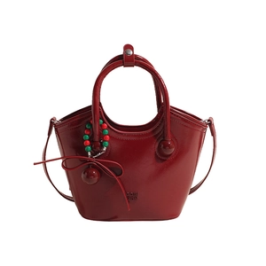 Sac seau en cuir bordeaux brillant avec poignées et bandoulière sur fond blanc épuré
