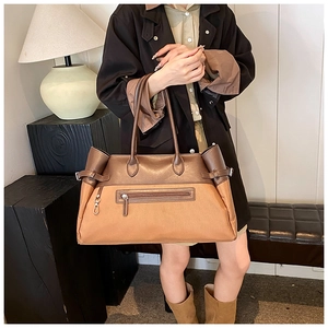 Detail of a brown leather patchwork tote bag featuring side buckles and a metal hook charm