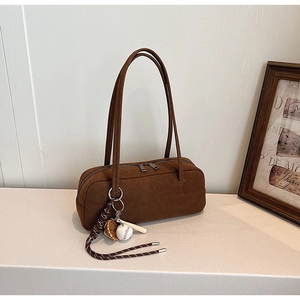 Nahaufnahme der braunen Wildleder-Baguette-Tasche mit Baseball-Anhänger auf Marmor