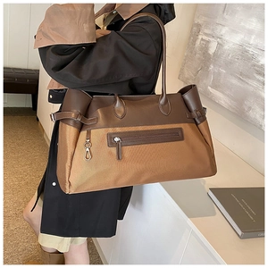 Detail of a large canvas and leather tote bag featuring a front zipper pocket and long handles