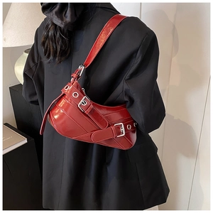 Close-up of a burgundy patent leather shoulder bag with decorative straps and silver buckles